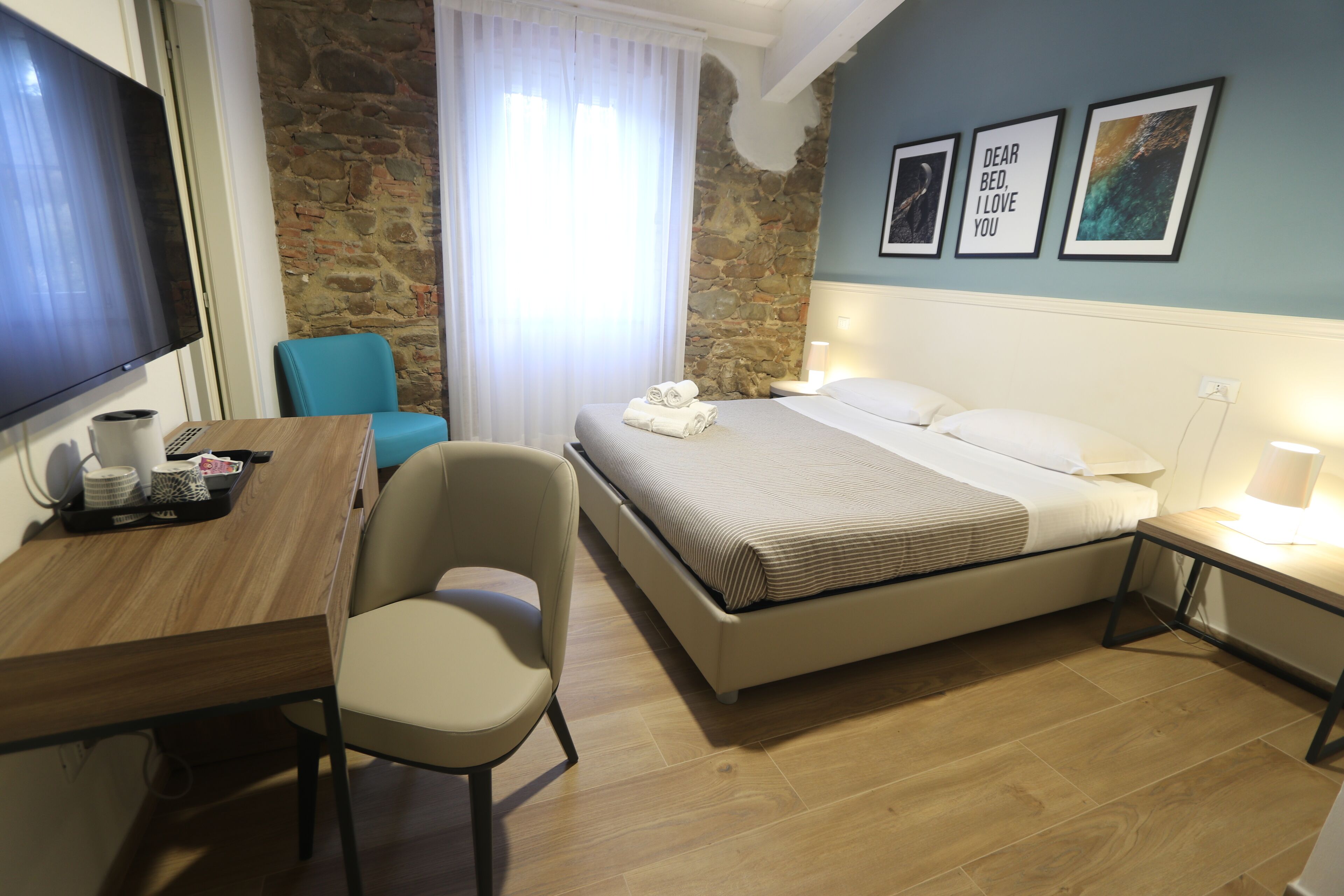 Habitación de hotel con cama, escritorio, silla, televisor y pared de piedra.