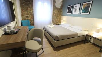 Habitación de hotel con cama, escritorio, silla, televisor y pared de piedra.