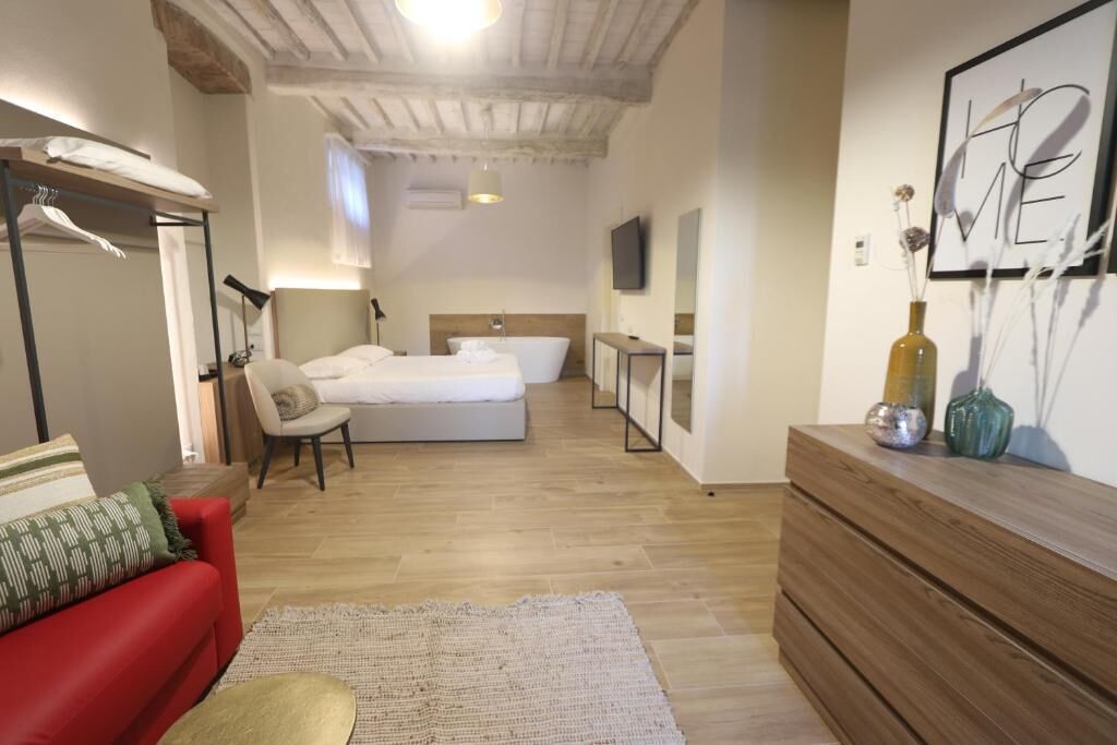 Una habitación de hotel con una cama, un sofá rojo, un aparador de madera y un televisor montado en la pared.