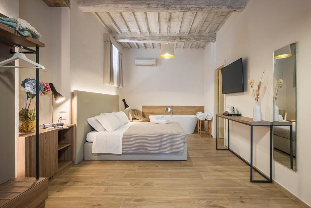 Ein modernes Schlafzimmer mit Holzboden, einem Bett mit weißer Bettwäsche, einem Nachttisch, einem Spiegel und einem an der Wand befestigten Fernseher.