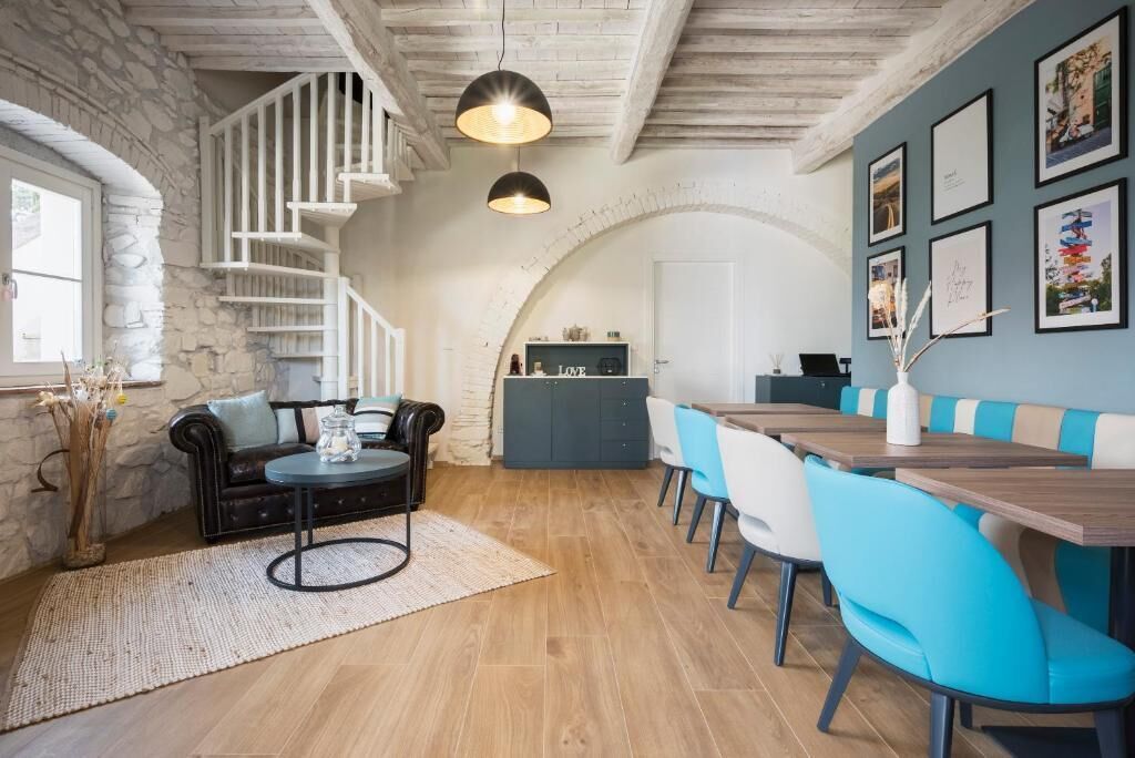 A dining area with a wooden table and blue chairs, a staircase with white railings, and a stone wall.