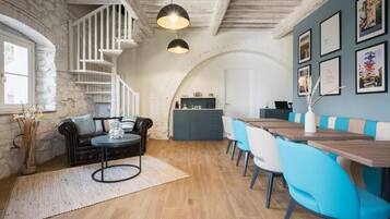 A dining area with a wooden table and blue chairs, a staircase with white railings, and a stone wall.