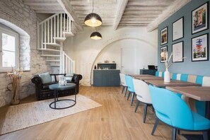 Un comedor con una mesa de madera y sillas azules, una escalera con barandillas blancas y una pared de piedra.