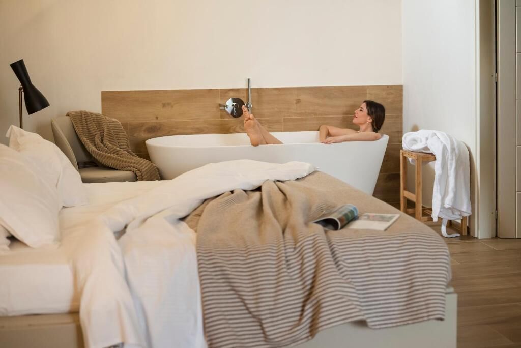 A bedroom with a large bathtub, a bedside table, and a lamp.
