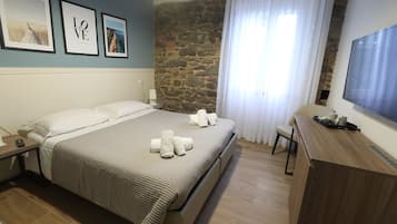 Relax in a spacious room with a large bed, flat-screen TV, and a desk, surrounded by framed artwork and sheer curtains.