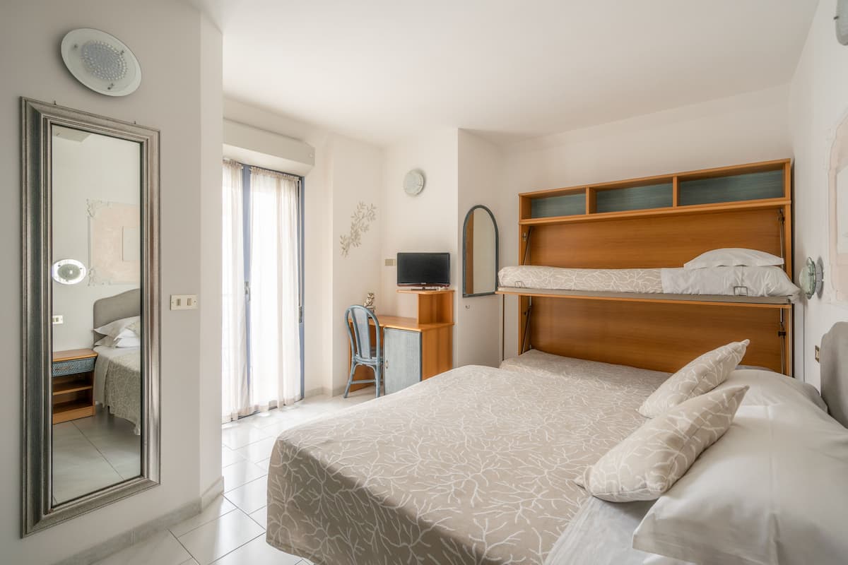 Habitación de hotel con literas, un escritorio, una silla, un espejo y una ventana con cortinas.
