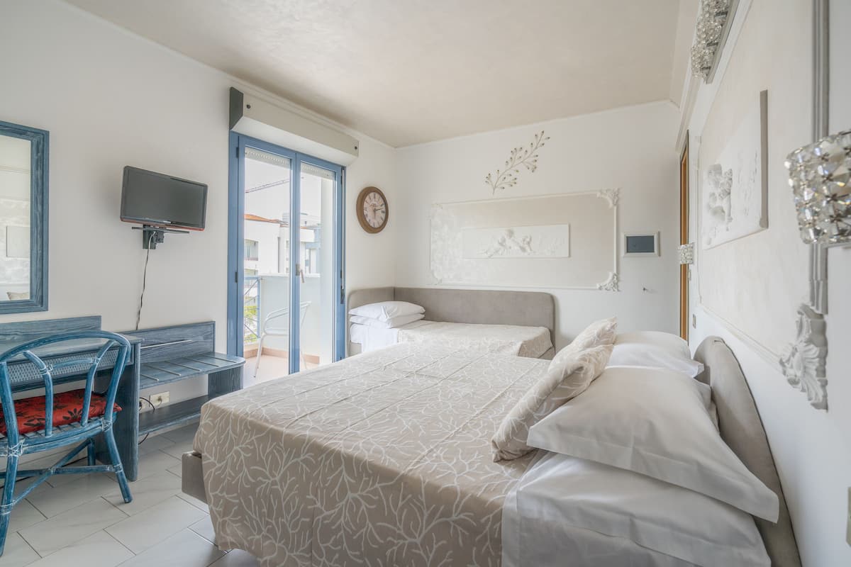 Habitación de hotel con cama, escritorio, silla, televisor y puerta que da a un balcón.