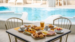 Une table à manger avec des aliments pour le petit-déjeuner et un verre de jus d’orange, placée au bord d’une piscine.
