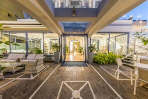 Eine moderne Hotelhalle mit Steinboden, Korbmöbeln und einem Glastürrahmen, der zu einer Treppe führt.