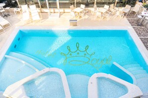 A swimming pool with a 'Royal' logo and white lounge chairs around it.