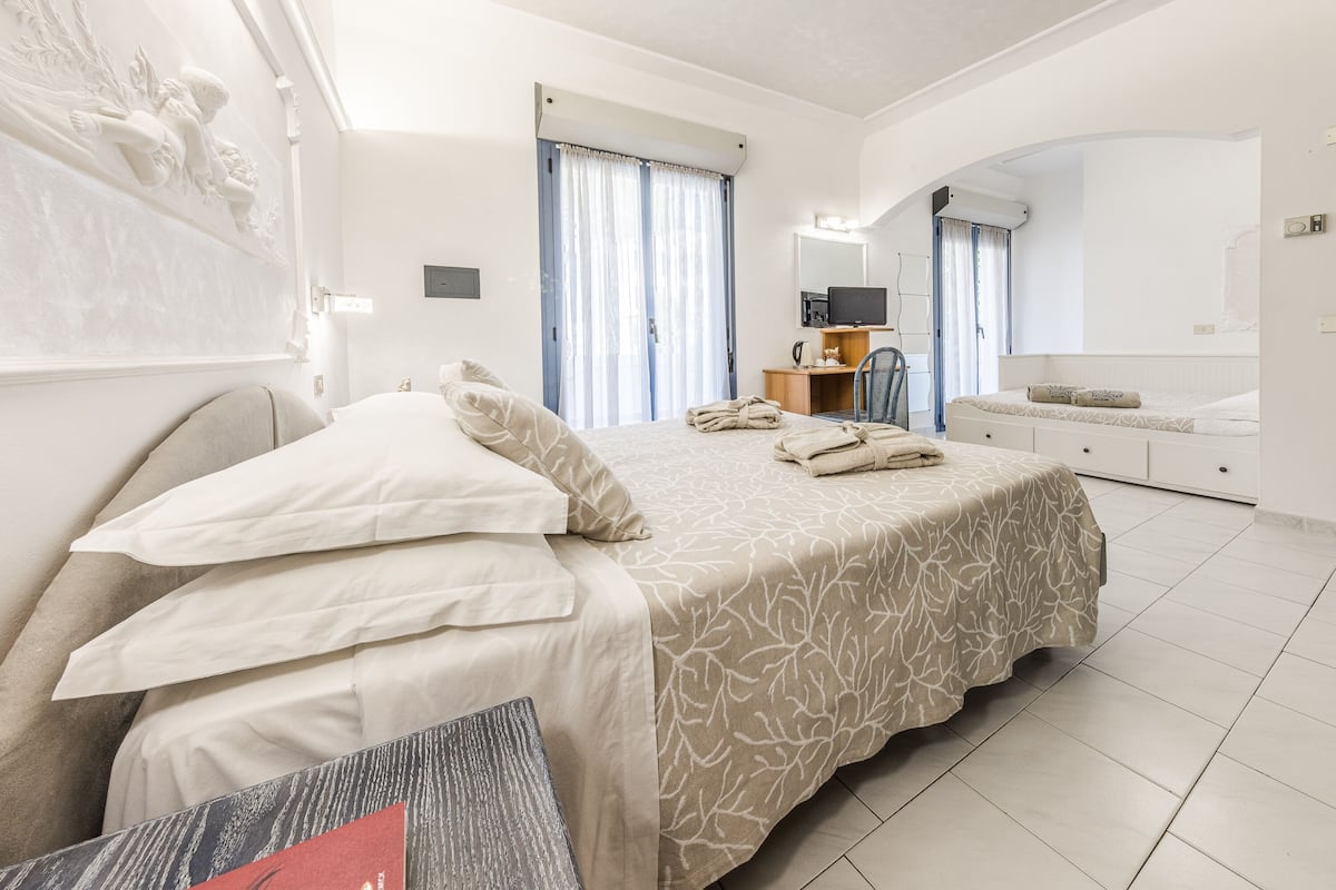 Habitación de hotel con una cama grande, un escritorio, una silla, un televisor y un baño con espejo y lavamanos.