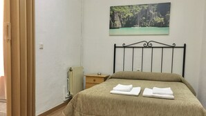 A bedroom with a bed, a nightstand, a radiator, and a painting of a coastal landscape. - Hostal Santa Bárbara (Toledo)