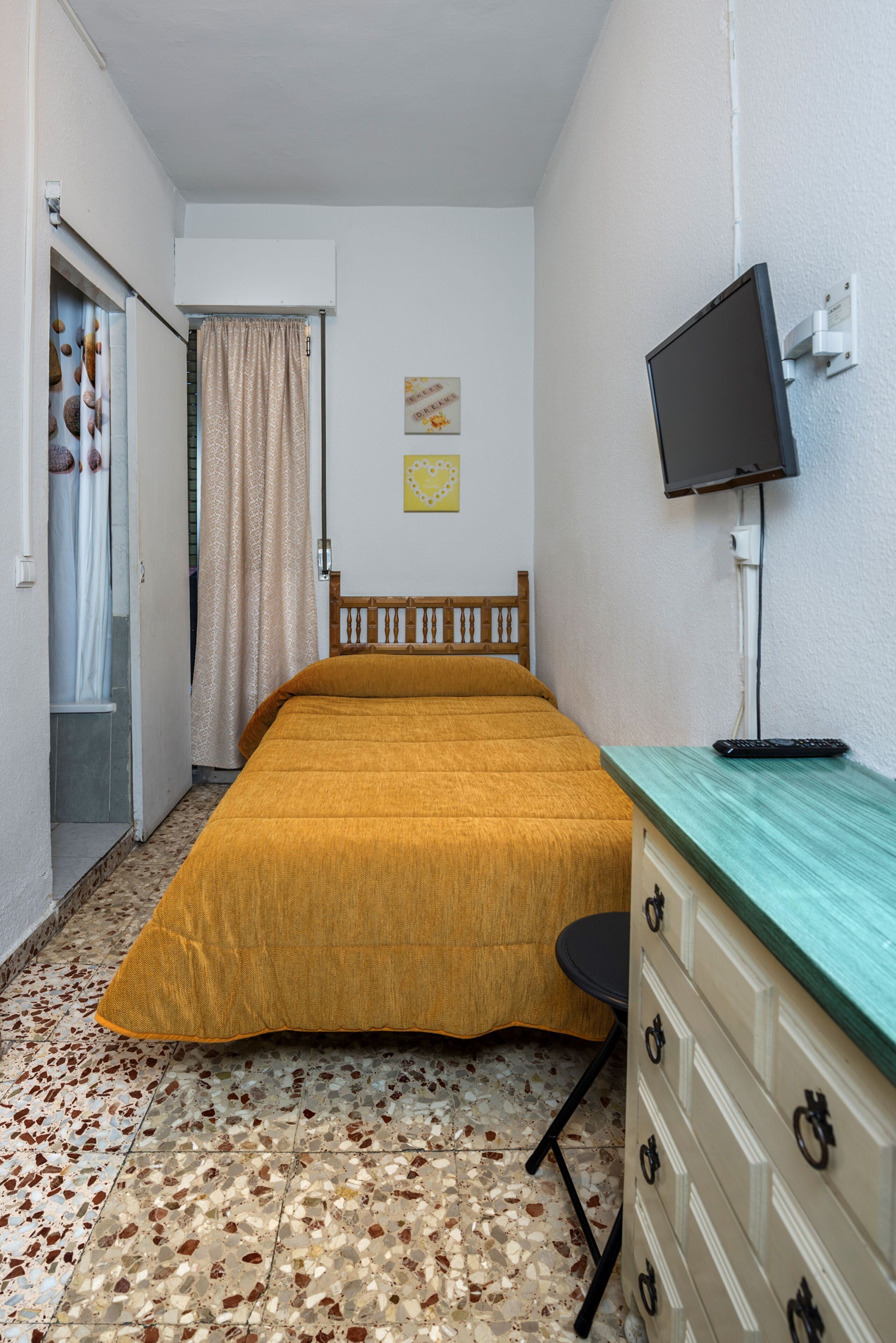 Una habitación pequeña con cama, escritorio, televisor y armario.