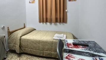 A small, sparsely furnished room with a bed, a table with a Union Jack tablecloth, a radiator, and a wall-mounted air conditioner.