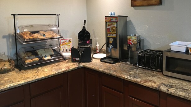 A breakfast station with a waffle maker, syrup dispenser, and a microwave. - Express Inn West Memphis (West Memphis)