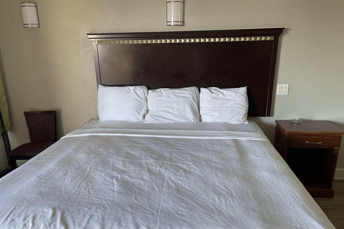 A hotel room with a large bed, a wooden nightstand, and a chair.