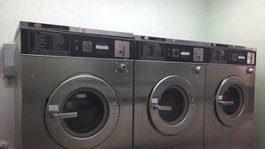 A row of stainless steel front-loading washers with control panels, located in a public laundry facility. - Express Inn West Memphis (West Memphis)
