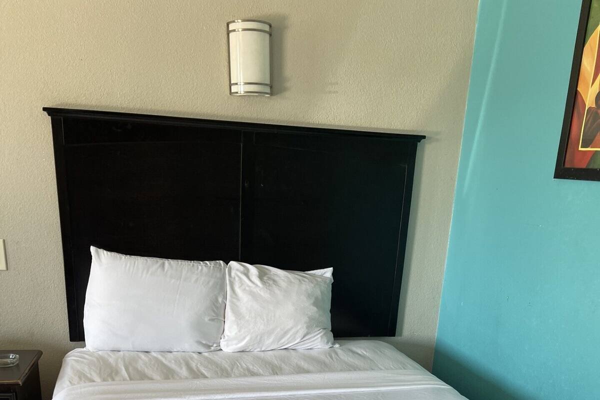 A neatly made bed with white linens in a room with a dark headboard and a light blue accent wall.