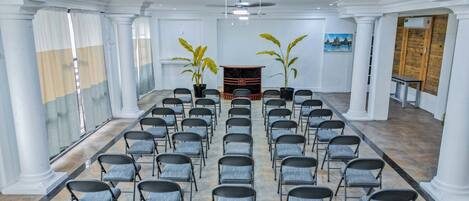 A conference room with rows of chairs, a ceiling fan, and two potted plants.
