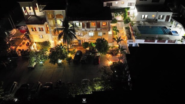 A nighttime view of a hotel courtyard with multiple buildings, a swimming pool, and parked cars. - SAMS Hotel (Port-au-Prince)
