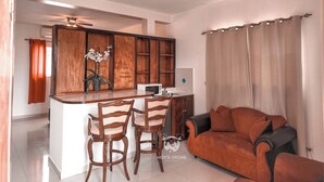 A modern kitchen with wooden cabinets, a central island with bar stools, a microwave, and a ceiling fan. - SAMS Hotel (Port-au-Prince)
