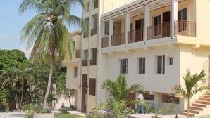 A multi-story residential building with balconies, surrounded by palm trees and greenery. - SAMS Hotel (Port-au-Prince)