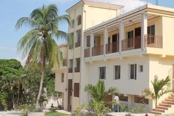 A multi-story residential building with balconies, surrounded by palm trees and greenery. - SAMS Hotel (Port-au-Prince)