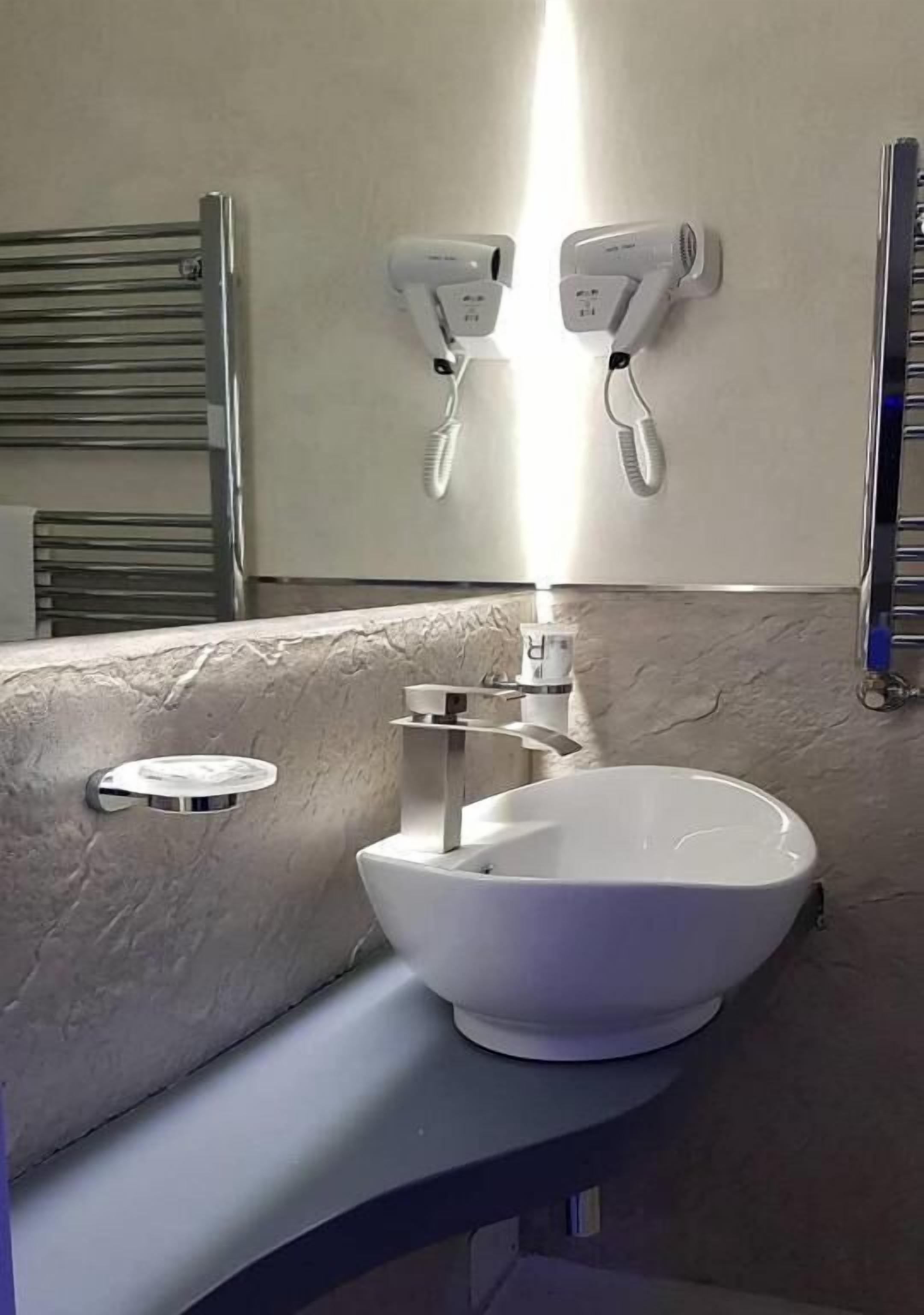 A bathroom with a white sink, a towel rack, and two wall-mounted hair dryers.