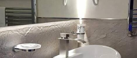 A bathroom with a white sink, a towel rack, and two wall-mounted hair dryers.