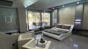 A modern living room with a large bed, a sofa, and a coffee table. There is a large window with a view of the outside. - Villa Rosa dei Venti (Cinisi)