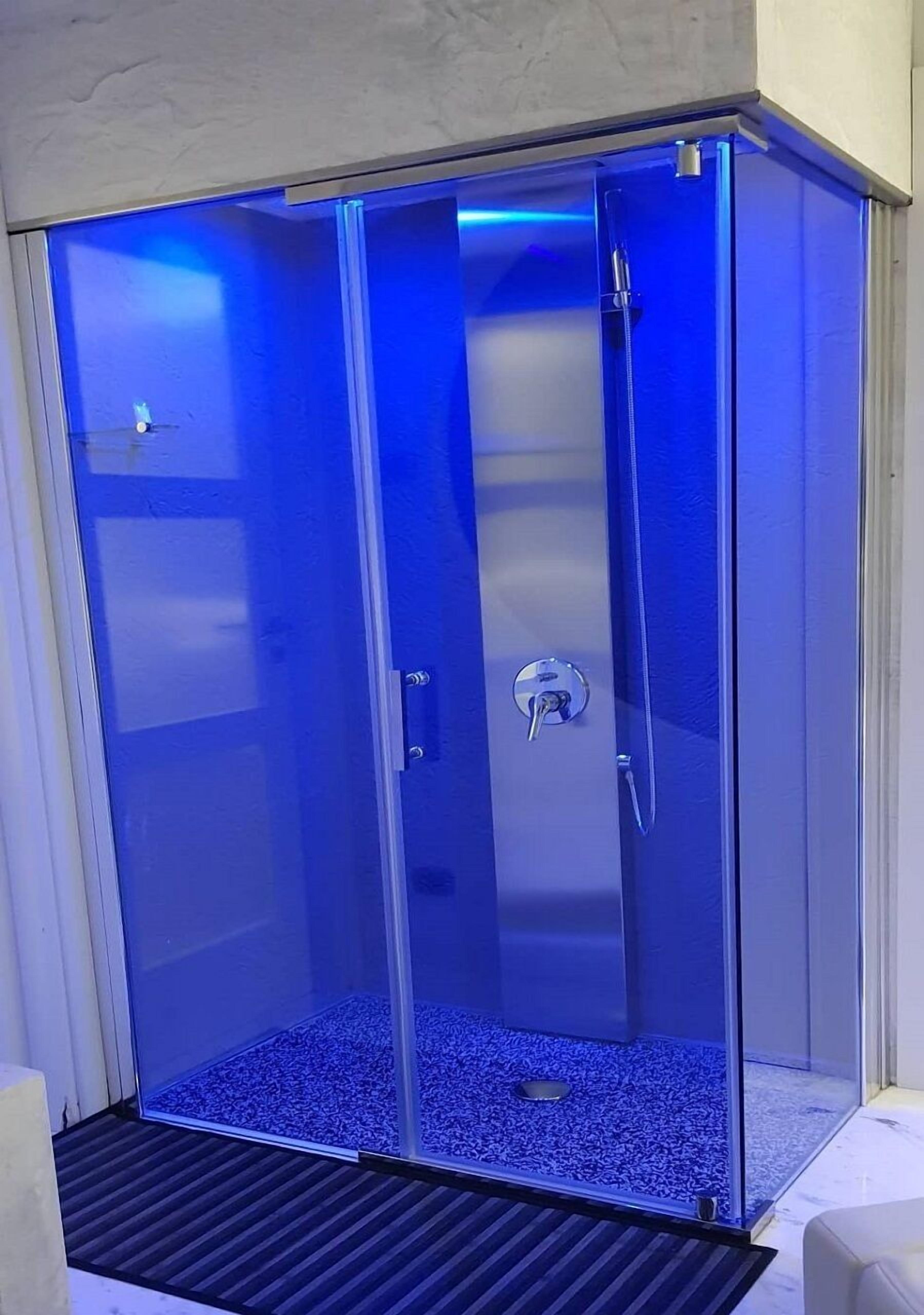 A glass-enclosed shower with a blue light, a metal door, and a drain.
