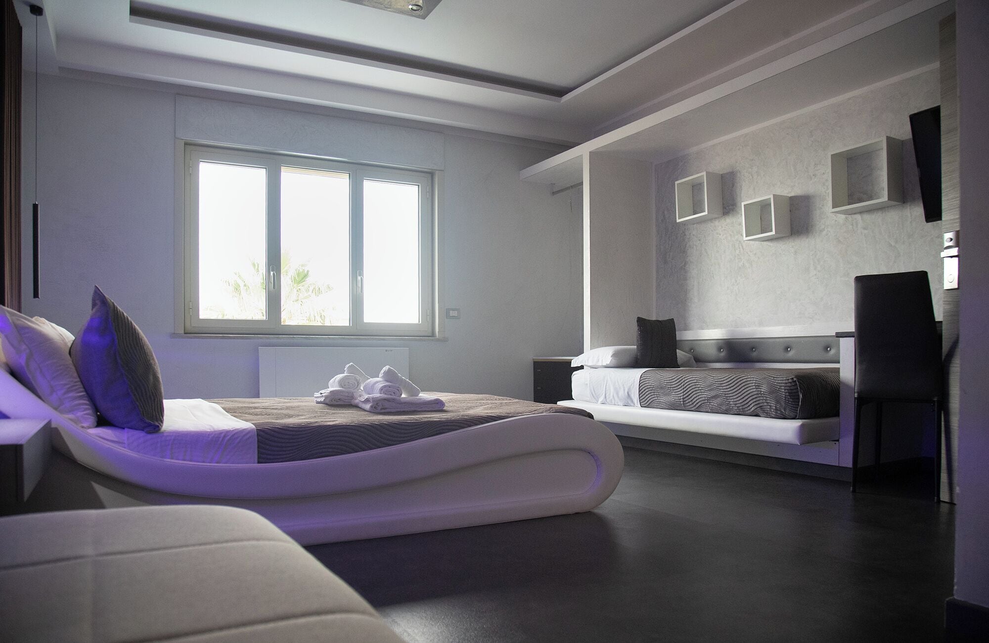 Une chambre moderne avec un lit, un canapé et un bureau. Une fenêtre laisse entrer la lumière naturelle.
