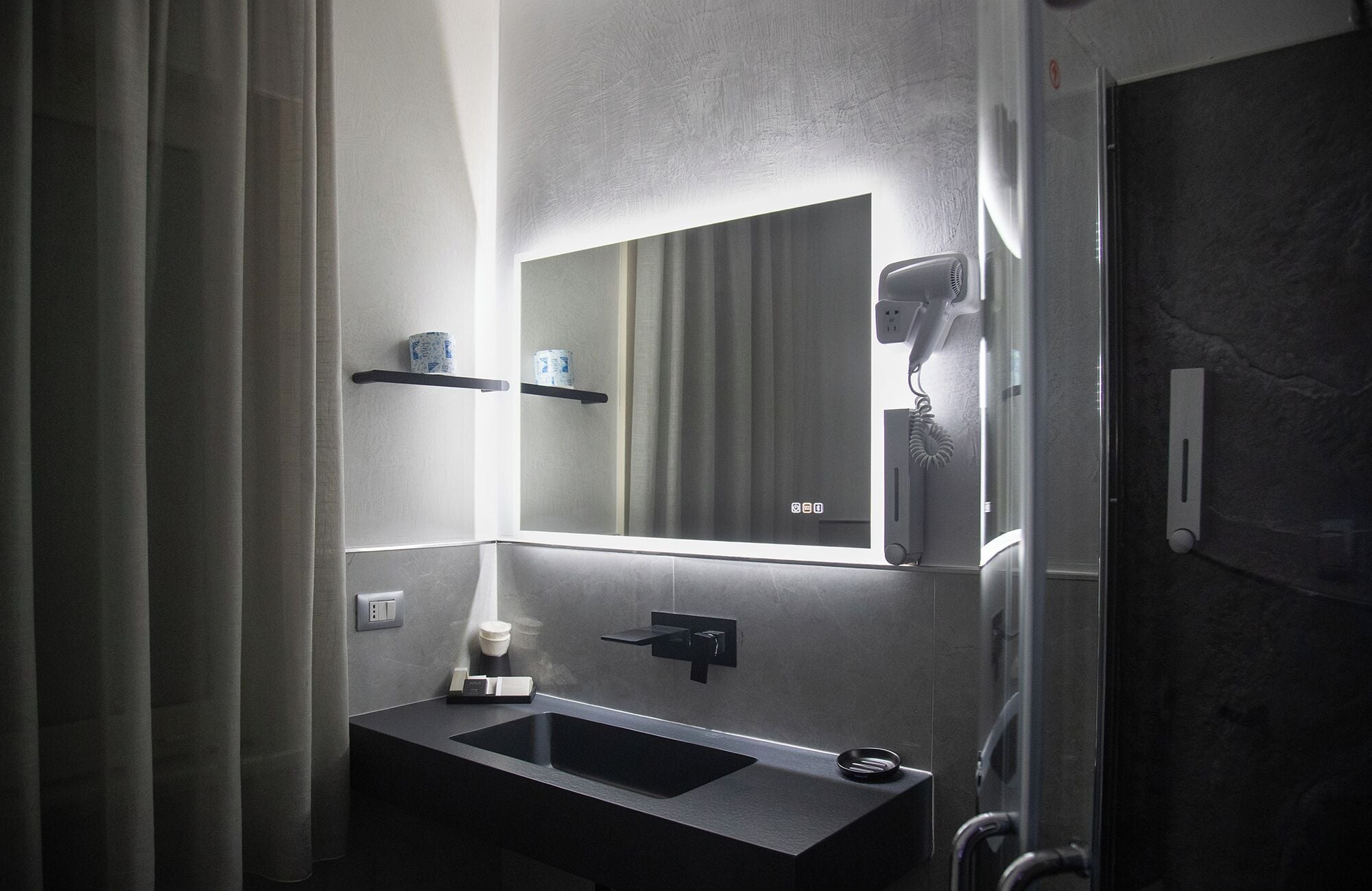 Un baño con un lavabo negro, un espejo, un secador de pelo y un perchero para toallas.