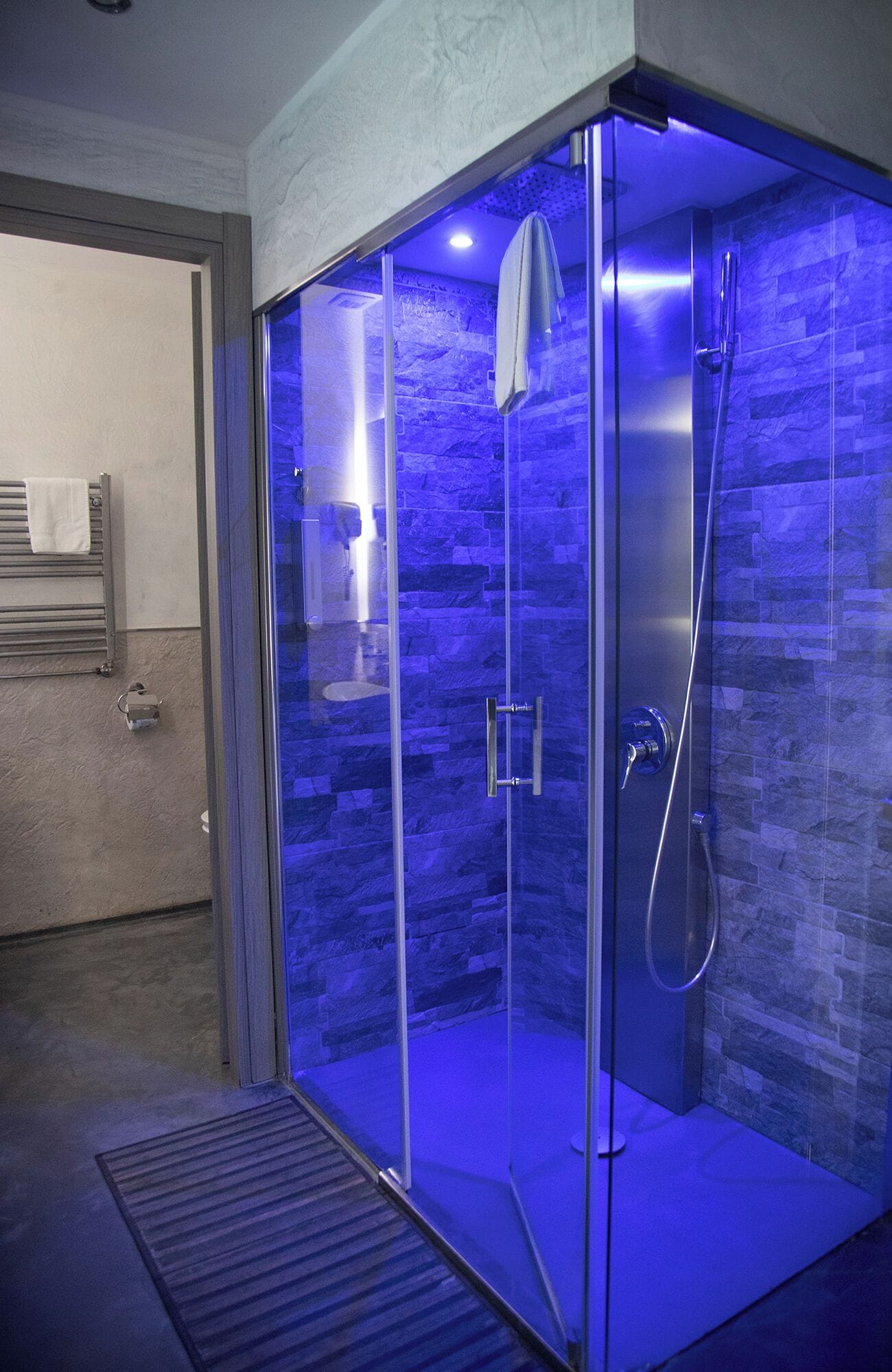 A glass-enclosed shower with a stone wall backdrop and a towel hanging on the door.
