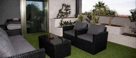 A rooftop patio with wicker furniture, a glass door, and potted plants.