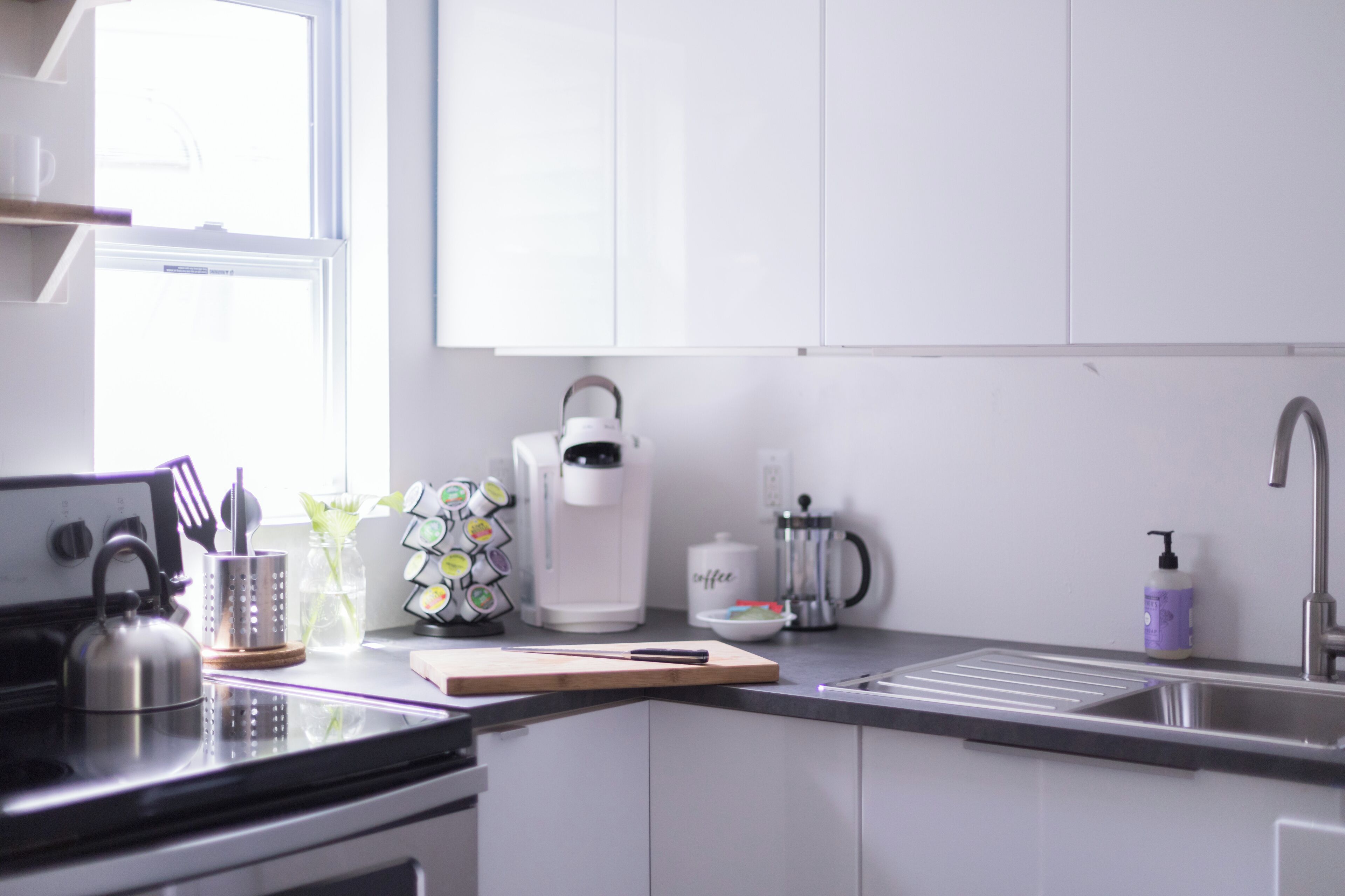 Una cocina moderna con armarios blancos, un hervidor, una cafetera y un lavamanos.