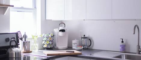 Una cocina moderna con armarios blancos, un hervidor, una cafetera y un lavamanos.