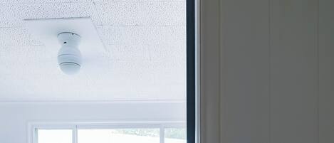Ett sovrum med en sängram i trä, ett fönster med utsikt över ett staket och ett tak med en lampa.