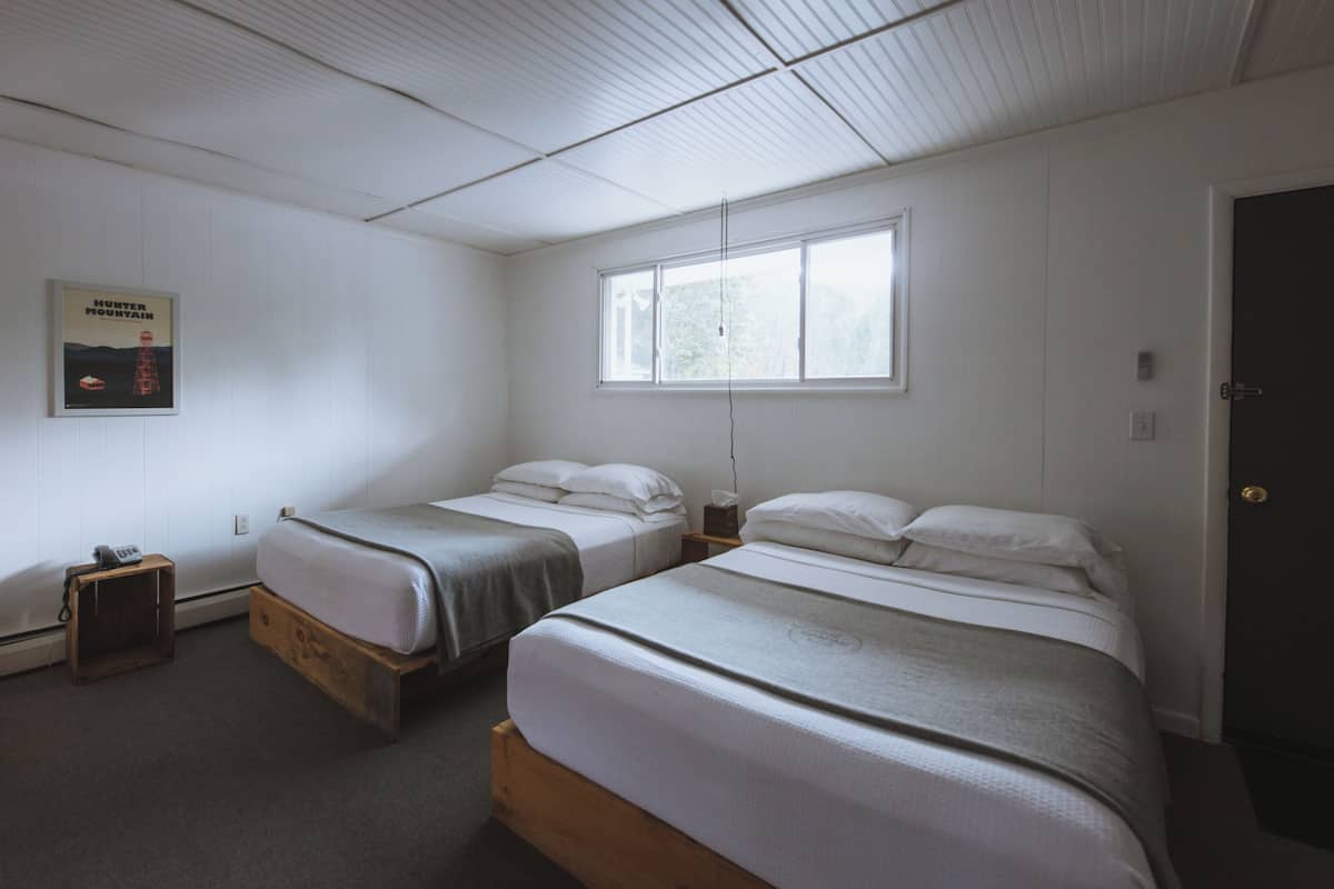 A room with two single beds, a wooden nightstand, a poster on the wall, and a window.