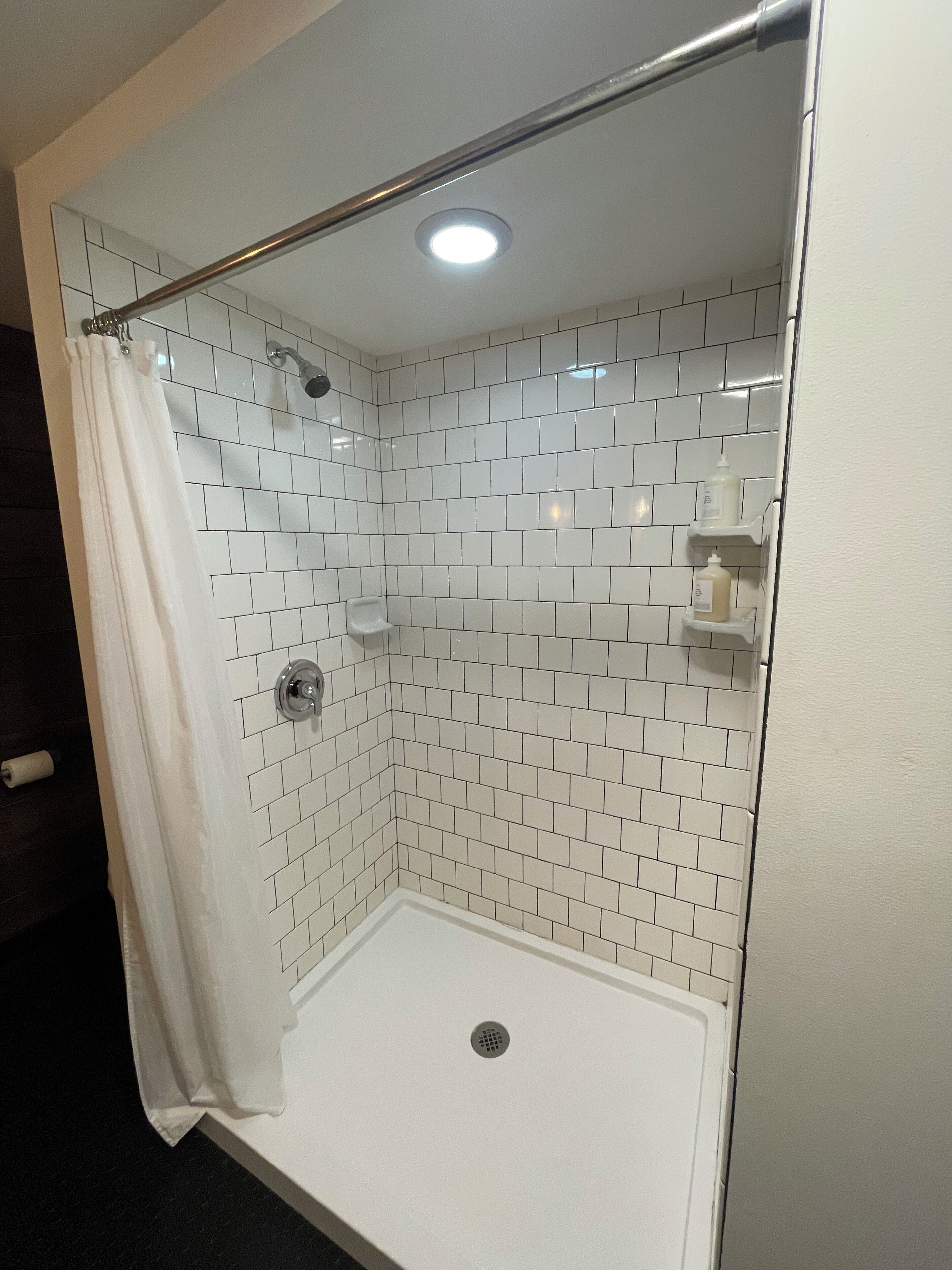 Een douche met witte betegelde wanden, een glazen deur en een metalen douchekop.