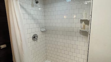 Een douche met witte betegelde wanden, een glazen deur en een metalen douchekop.