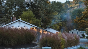 A rustic cabin with a chimney, surrounded by dense trees and a gravel driveway. - The Graham & Co. (Phoenicia)