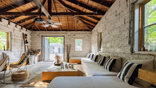 A rustic room with exposed brick walls, a wooden ceiling, a sofa set, a dining table, and a chair. - The Graham & Co. (Phoenicia)
