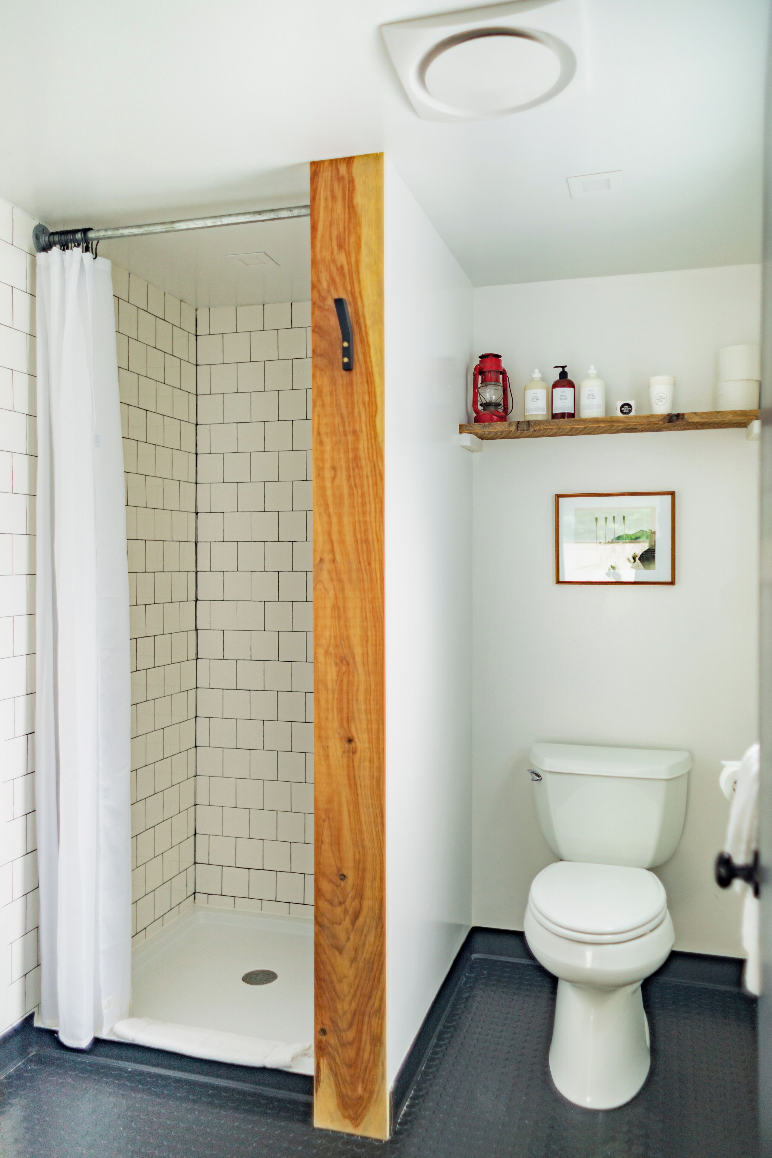Un baño con ducha, inodoro y estante con artículos de aseo.