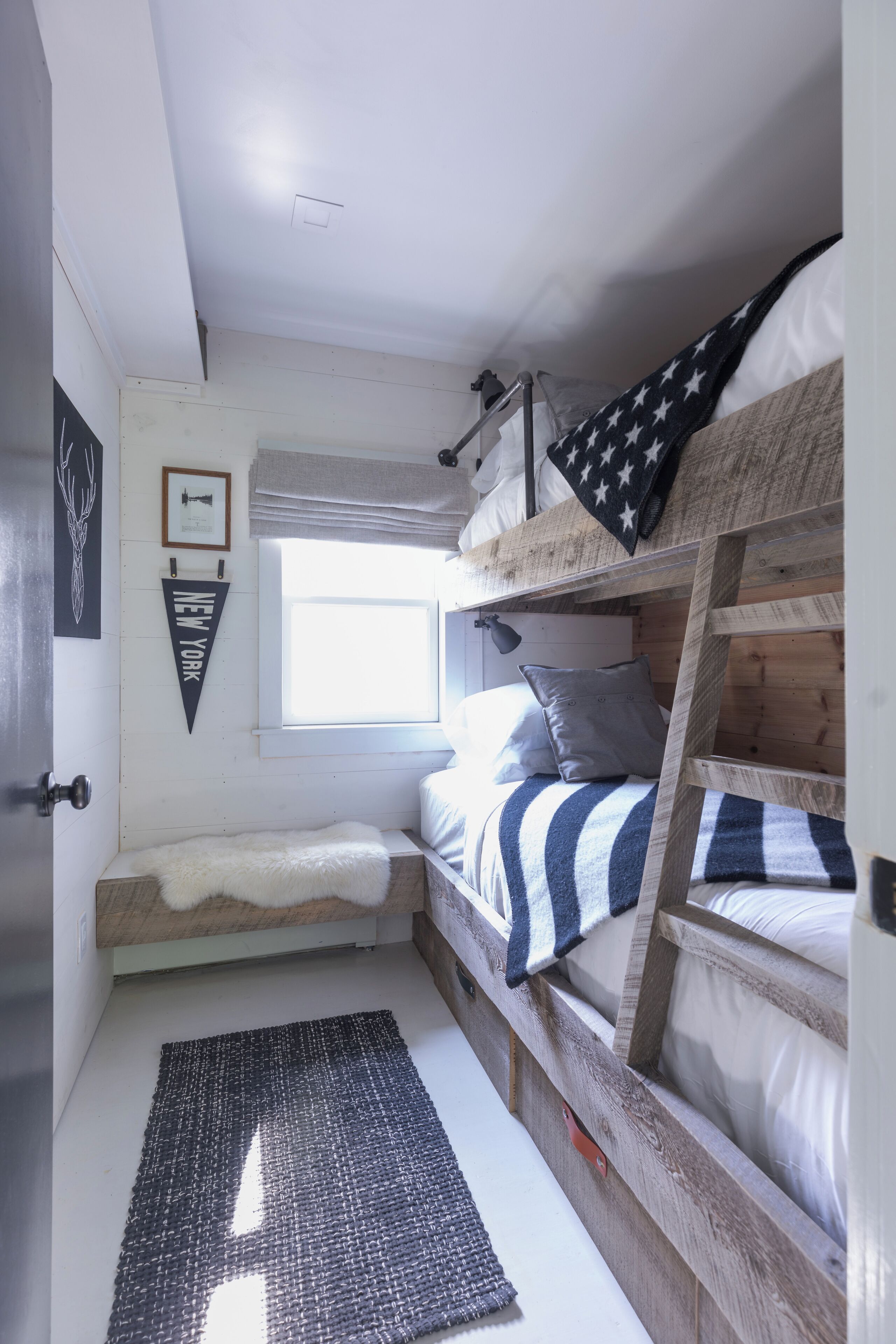 A compact bedroom with a bunk bed, a small window, a framed picture, and a rug.