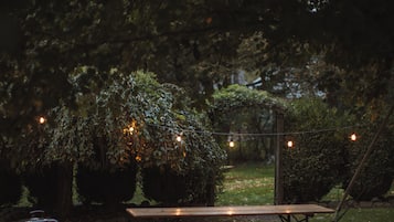 Ein Picknicktisch in einem Garten, umgeben von Bäumen und Sträuchern, mit Lichterketten beleuchtet.