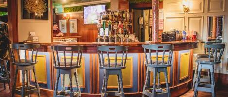 A bar area with a counter, bar stools, and a television screen.