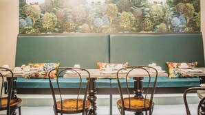 Een restaurant met een groene, gewatteerde bank, houten stoelen en een muurschildering van bomen.