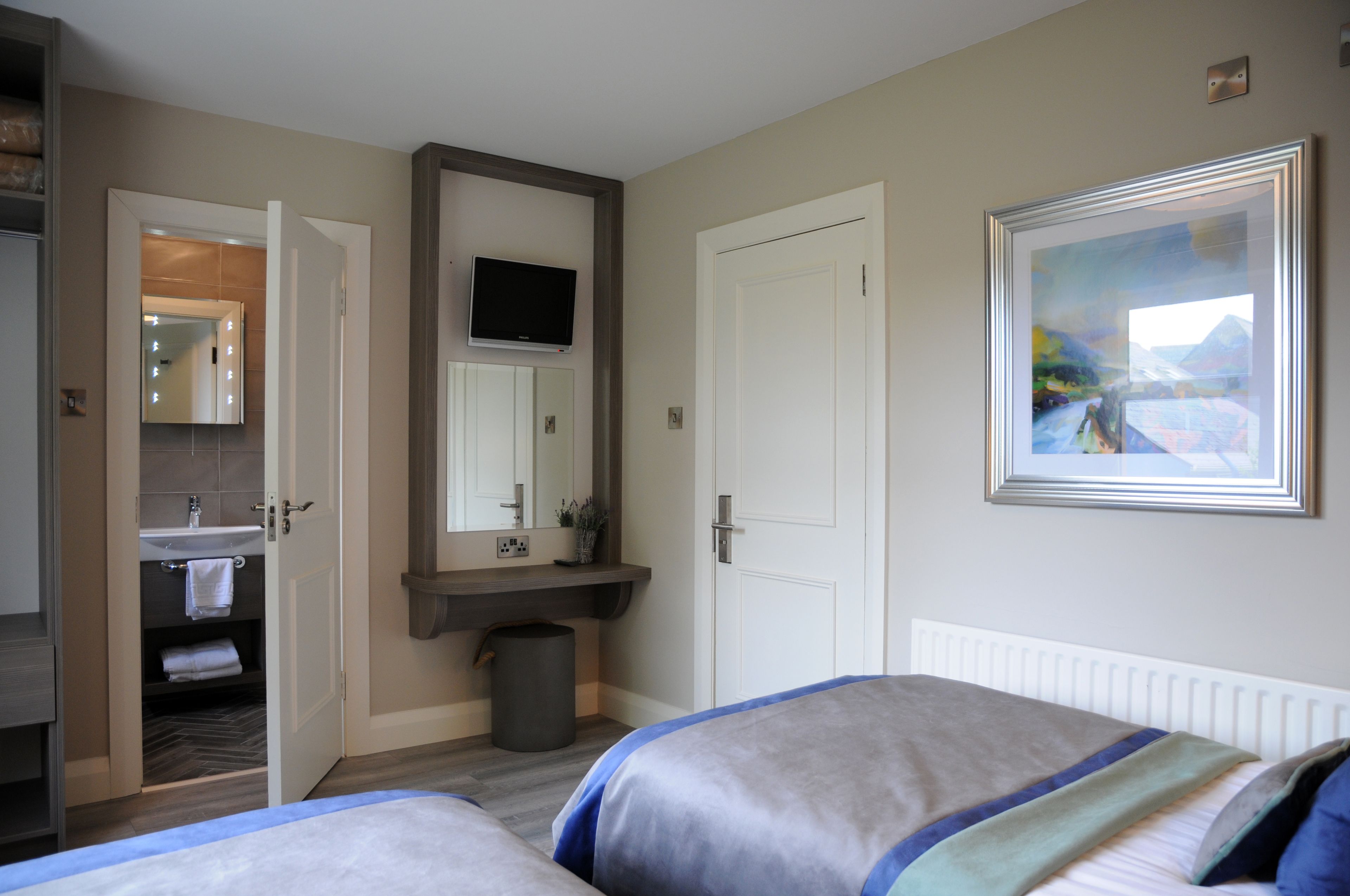 A hotel room with two beds, a bathroom with a sink and mirror, and a painting on the wall.