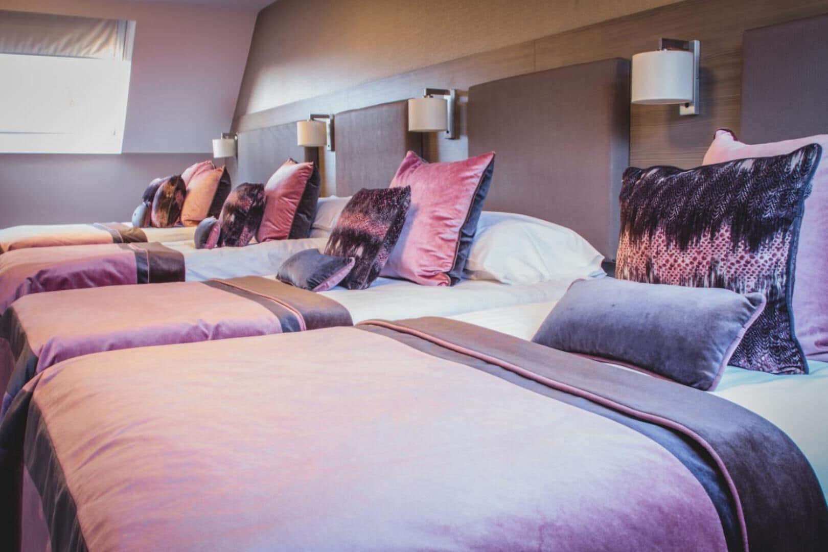 Habitación de hotel con varias camas, cada una con cabecero y lámparas de noche.